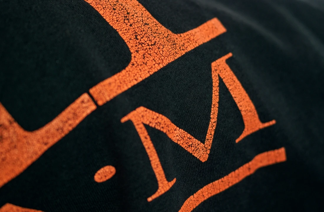 Close-up of a cracked orange graphic on black fabric illustrating print durability in a screen printing vs DTF comparison