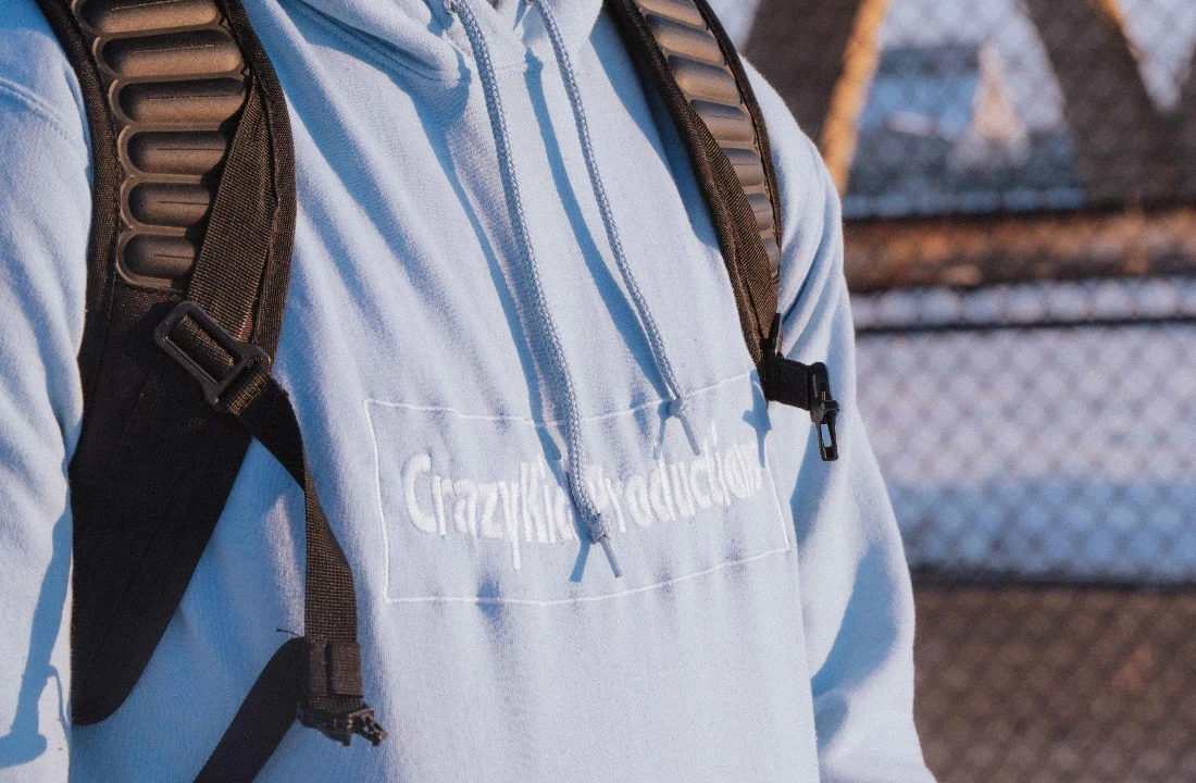 Light blue embroidery hoodie with a subtle tonal embroidered logo worn with a black backpack