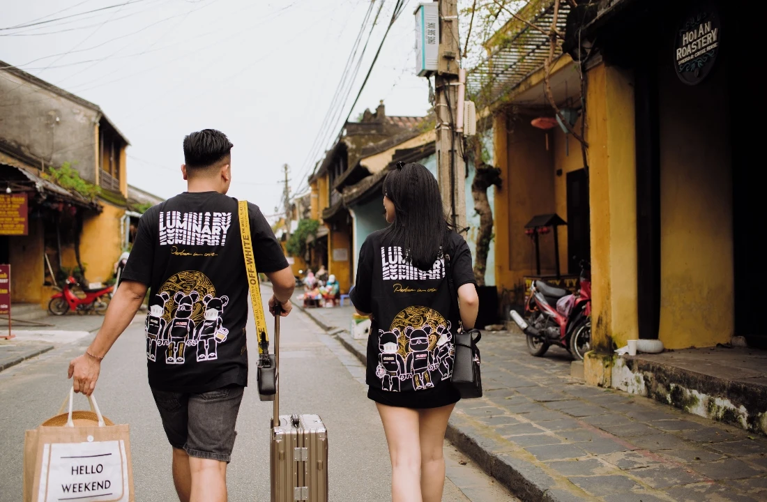 Two people walking through an old town in matching black T-shirts with large Jumbo Print back graphics