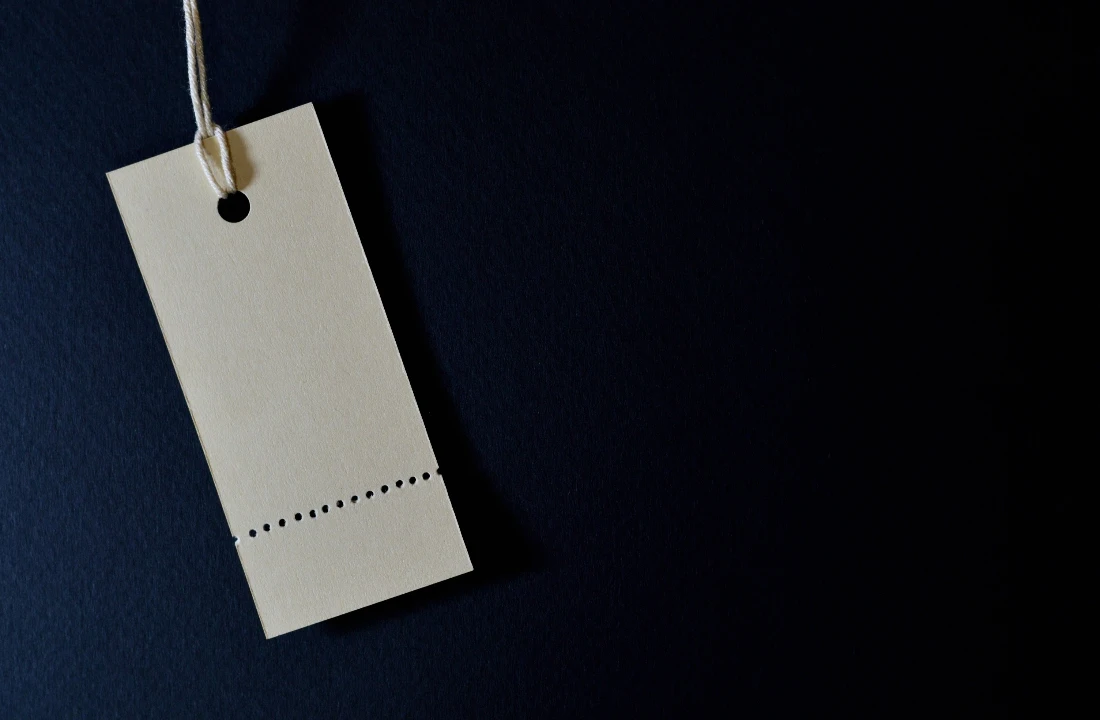 Blank rectangular custom clothing label attached with string against a dark fabric background