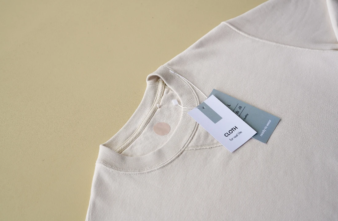 Custom clothing labels with branding and garment information attached to a cream crewneck sweatshirt