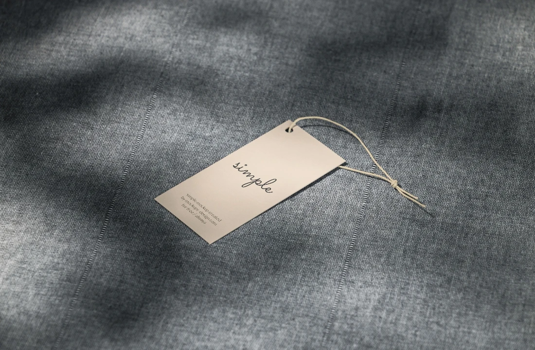 Beige custom clothing label with string placed on textured grey fabric for apparel branding and packaging