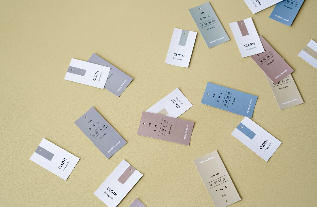 Collection of custom clothing labels featuring brand names, garment sizes and care symbols on a neutral background