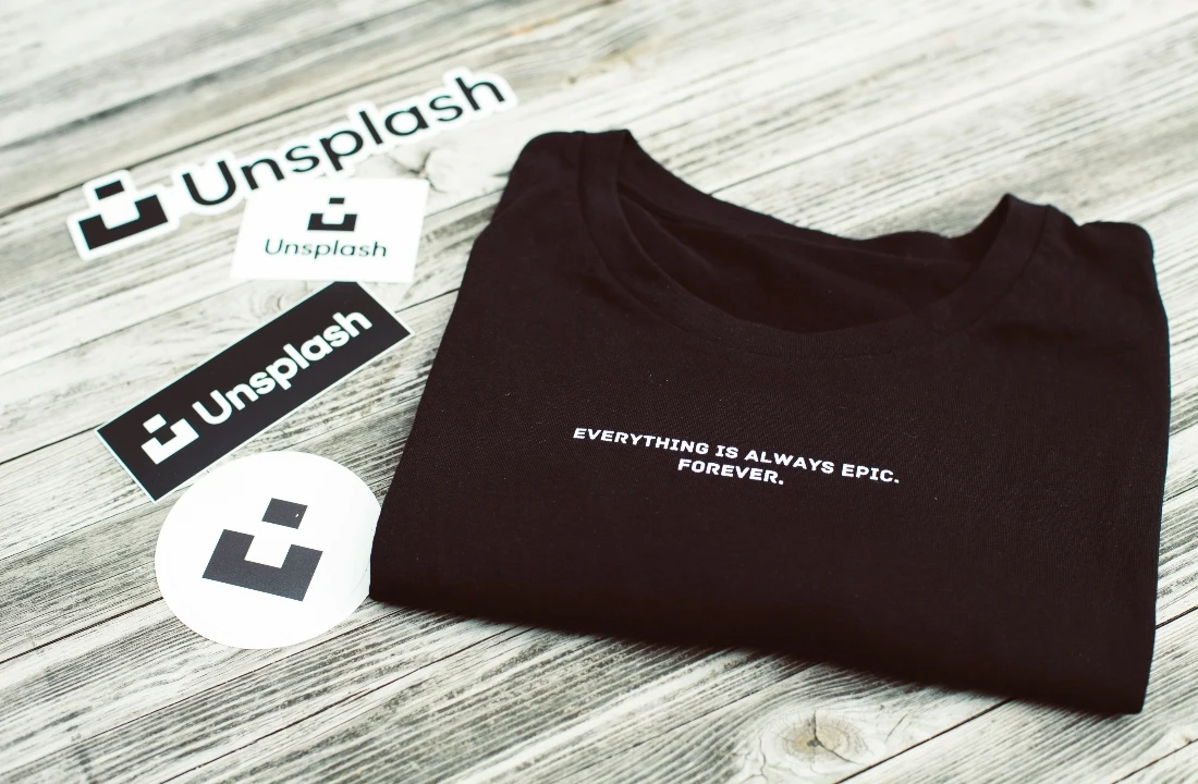 Folded black branded T-shirt displayed with matching stickers and inserts as a custom packaging presentation