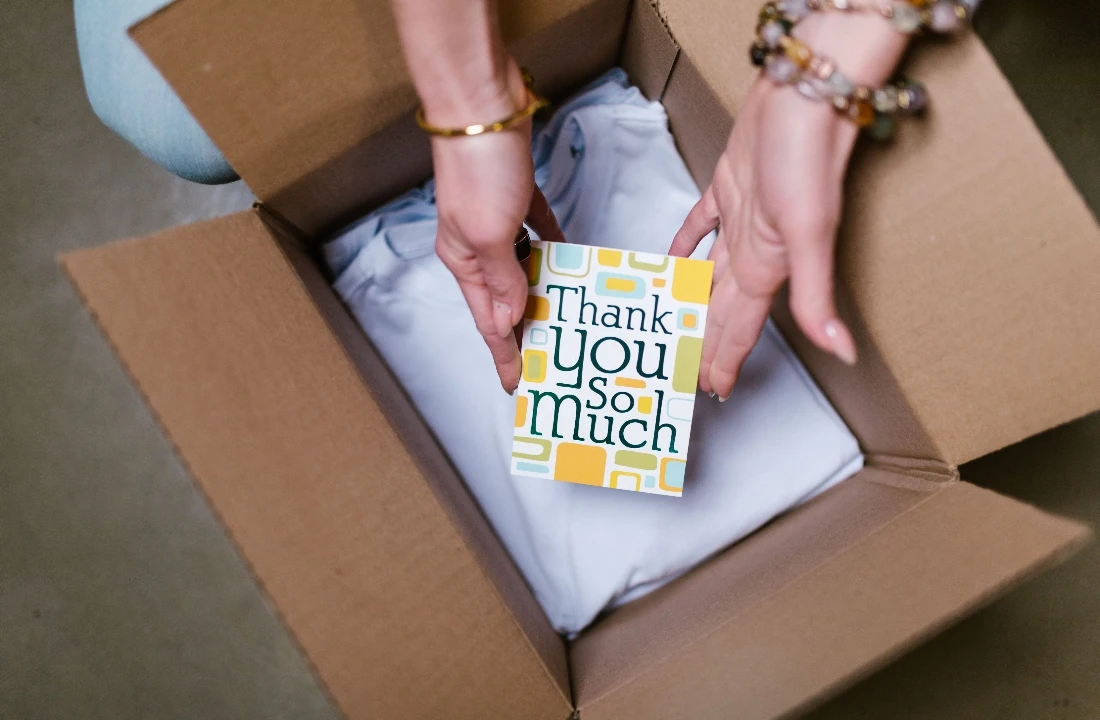 Hands adding a thank-you card to a boxed clothing order as part of a custom packaging experience