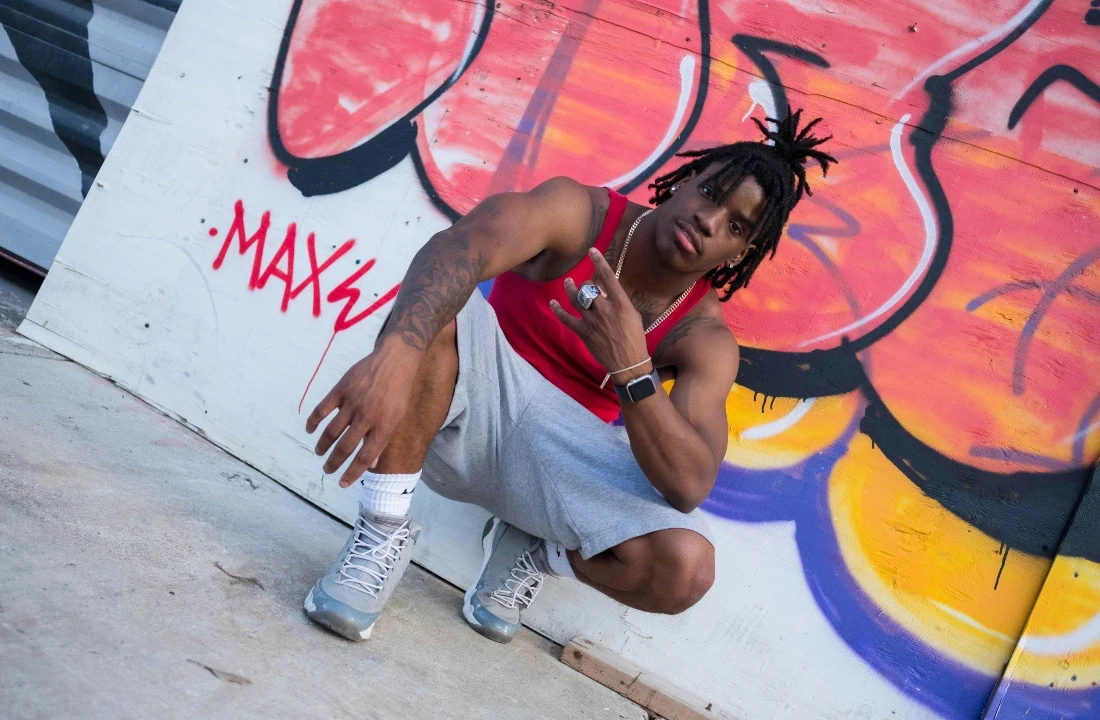 Man wearing a red tank top and relaxed grey Streetwear Shorts while posing in front of a colorful graffiti wall