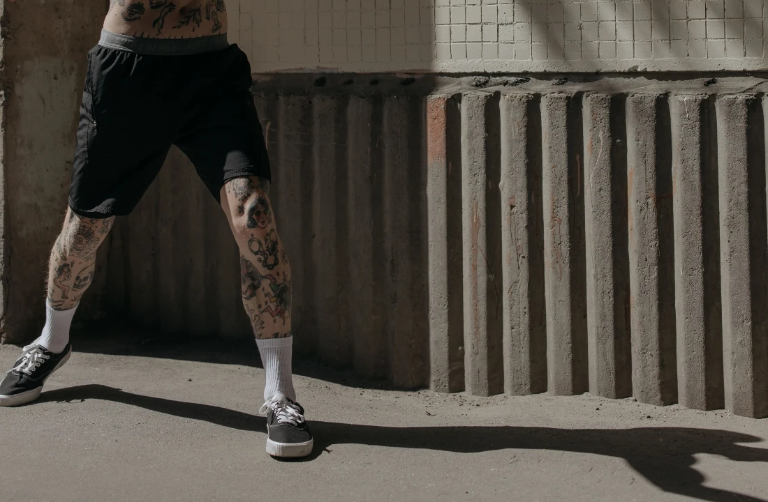 Tattooed model wearing relaxed black Fleece Shorts with white socks and sneakers in an industrial setting
