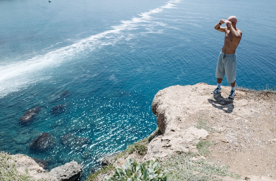 Man wearing loose grey Fleece Shorts with a drawstring waist while standing on a coastal cliff