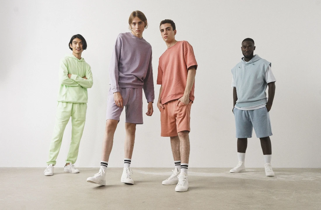 Four models wearing coordinated pastel sweatshirts, hoodies and Fleece Shorts in a studio setting