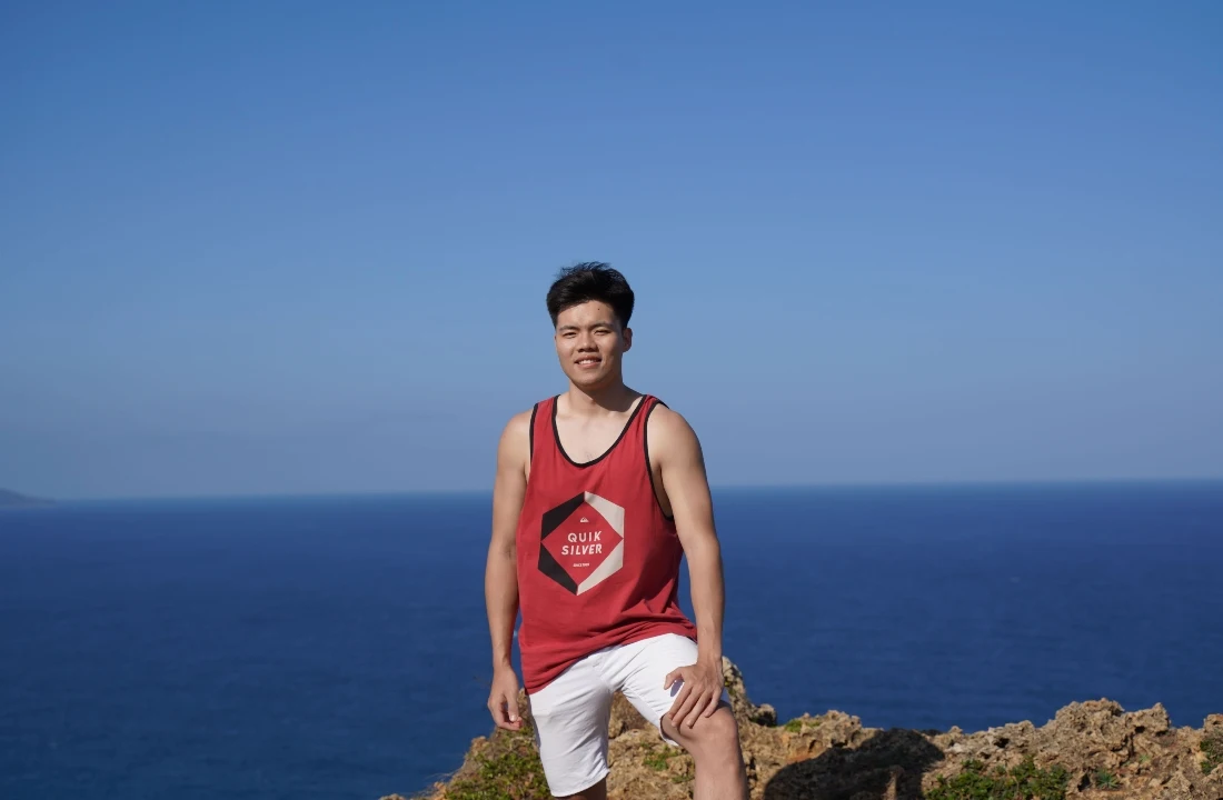 Man wearing a red Custom Tank Top with a geometric logo print and white shorts near the coast