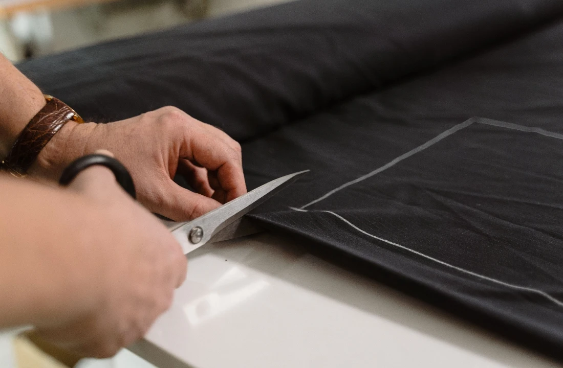 Tailor cutting black fabric along marked pattern lines during the Custom Apparel production process