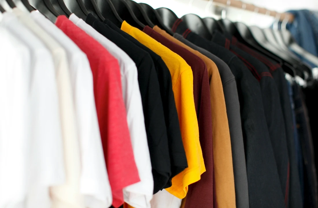 Assorted blank Custom Apparel T-shirts in white, red, yellow, brown and black hanging on a clothing rack