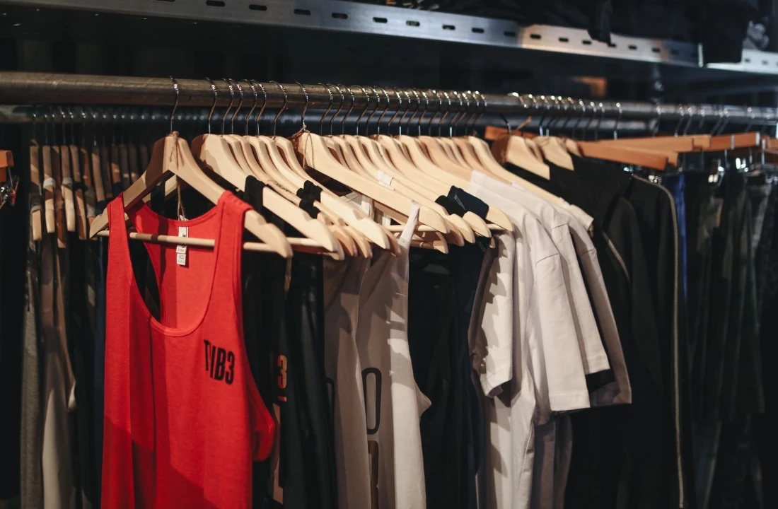 Custom Apparel tank tops and T-shirts displayed on wooden hangers inside a clothing store