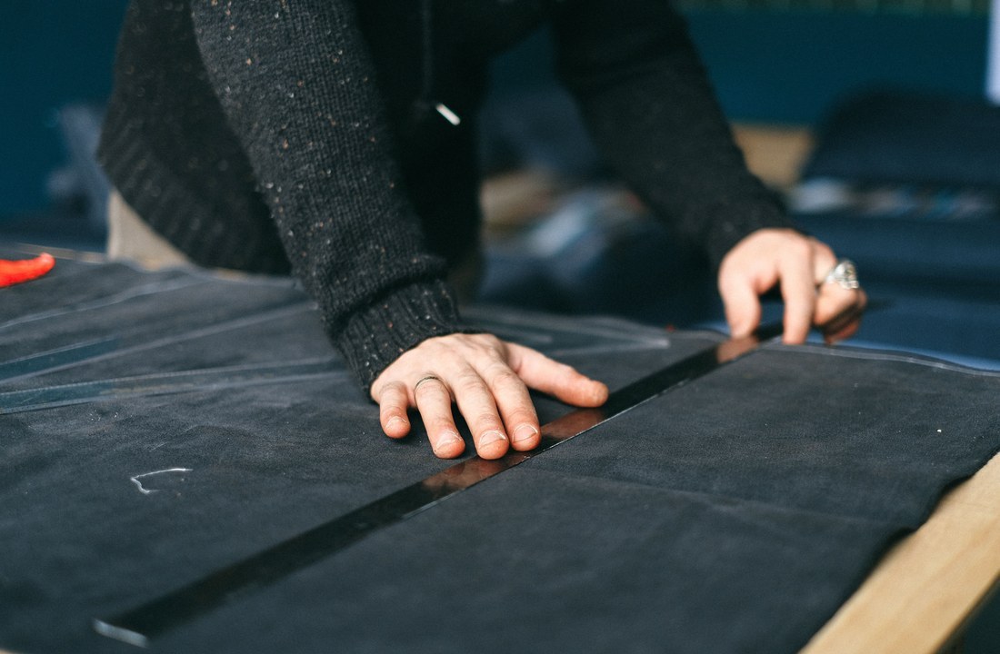 Hands measuring dark fabric for a holiday apparel production calendar