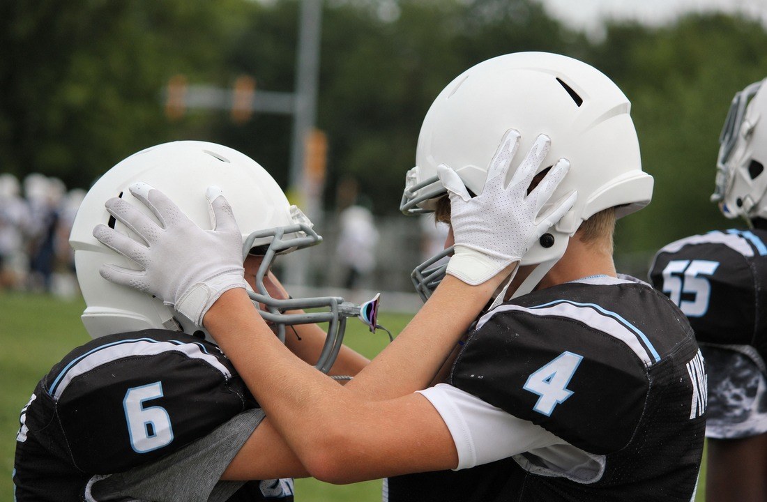 Two football teammates in coordinated uniforms holding their helmets