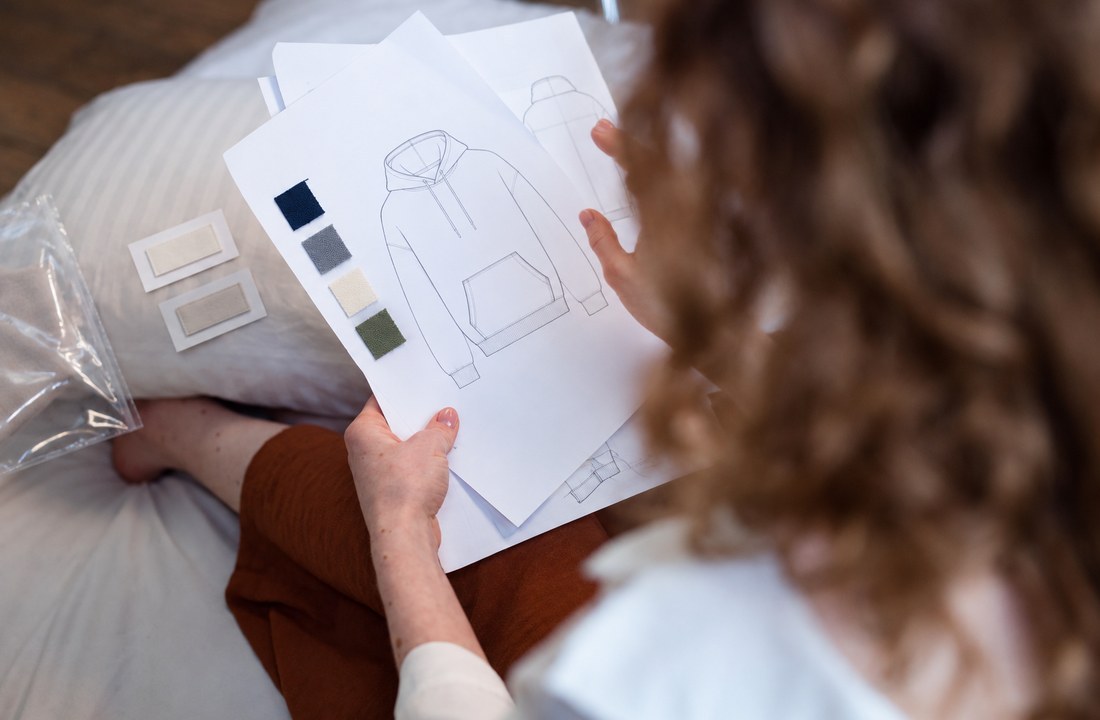Designer reviewing a blank hoodie sketch with fabric and label samples