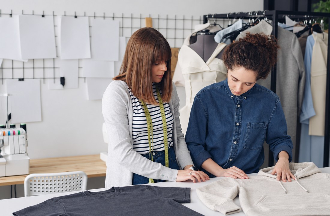 Two apparel developers reviewing plain T-shirt and hoodie samples in a workshop