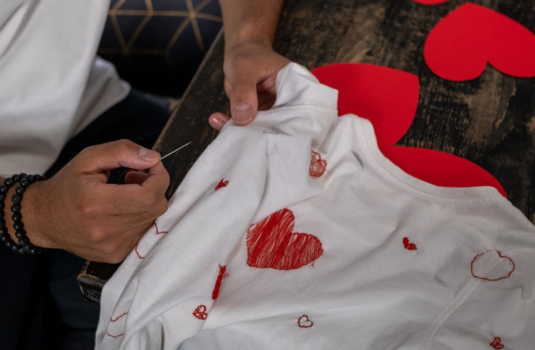 Hands stitching red hearts onto a white garment