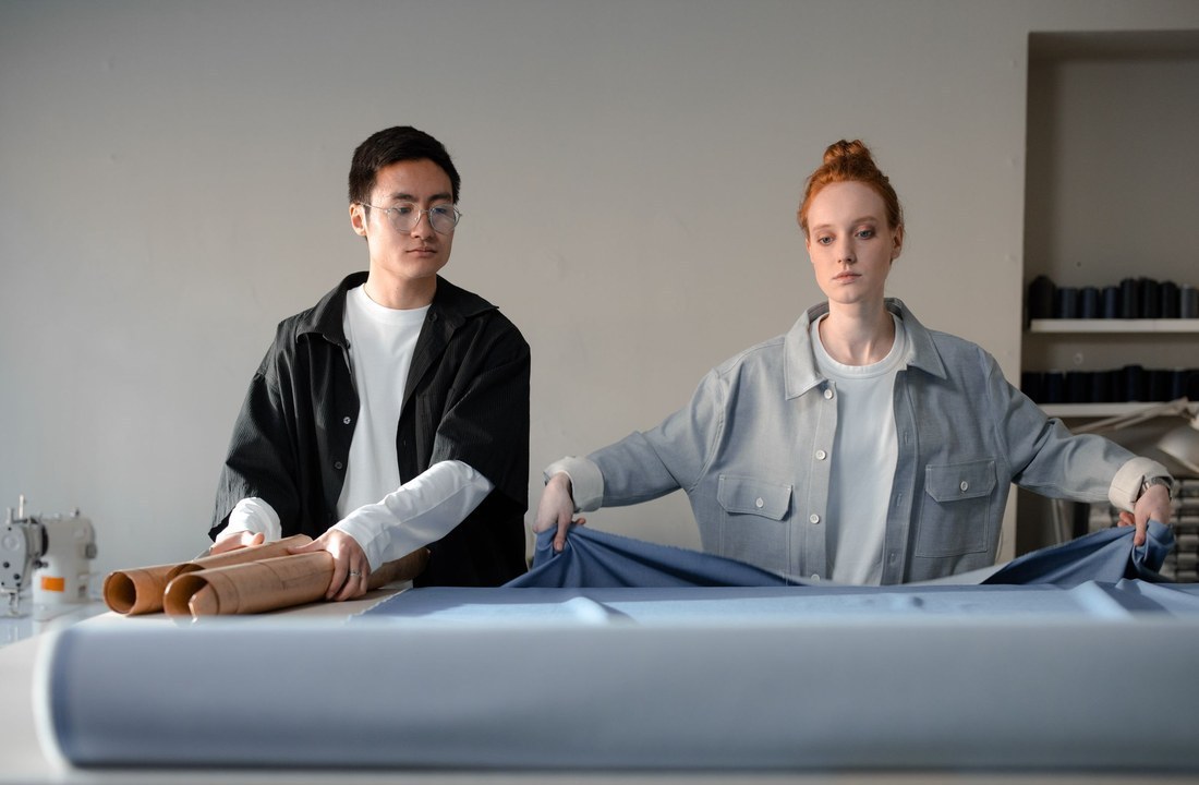 Two garment workers reviewing fabric on a table