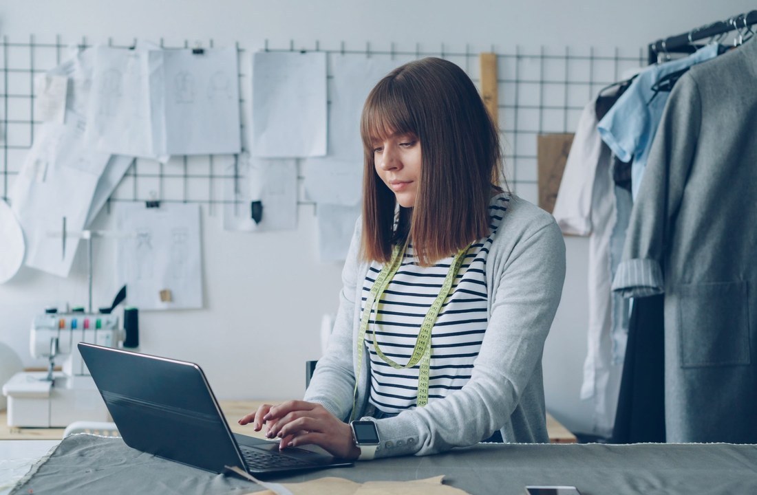 Designer working at a desk with garments on a rack