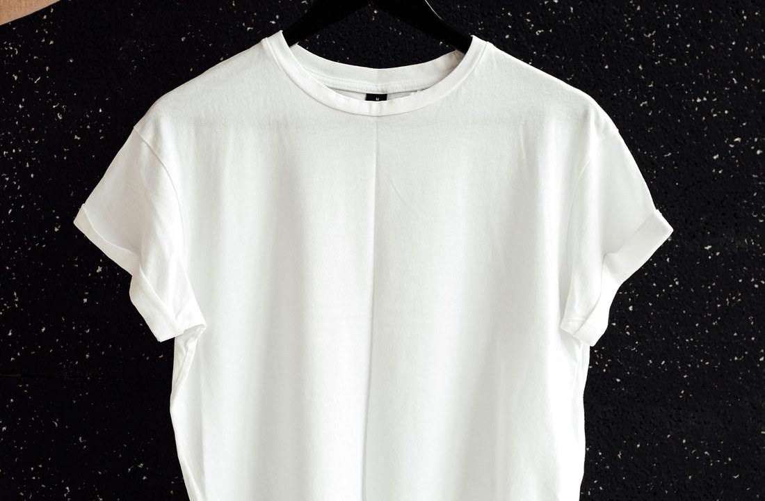 Plain white T-shirt held on a hanger against a dark wall