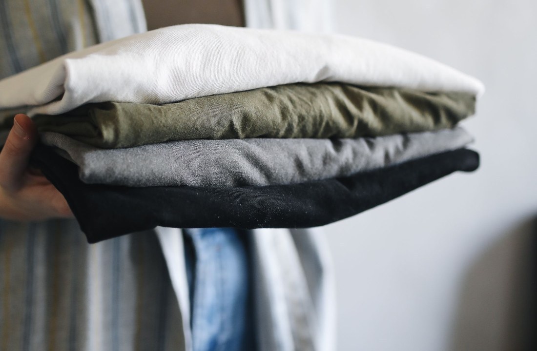 Person holding four folded garments in different neutral colors