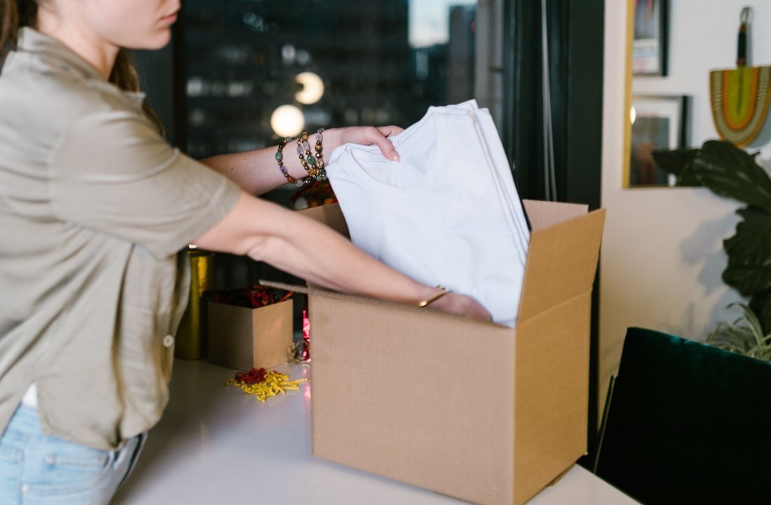 Person placing folded white T-shirts into a cardboard box