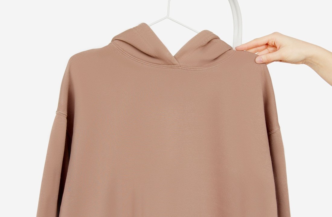 Person holding a plain brown pullover hoodie on a hanger