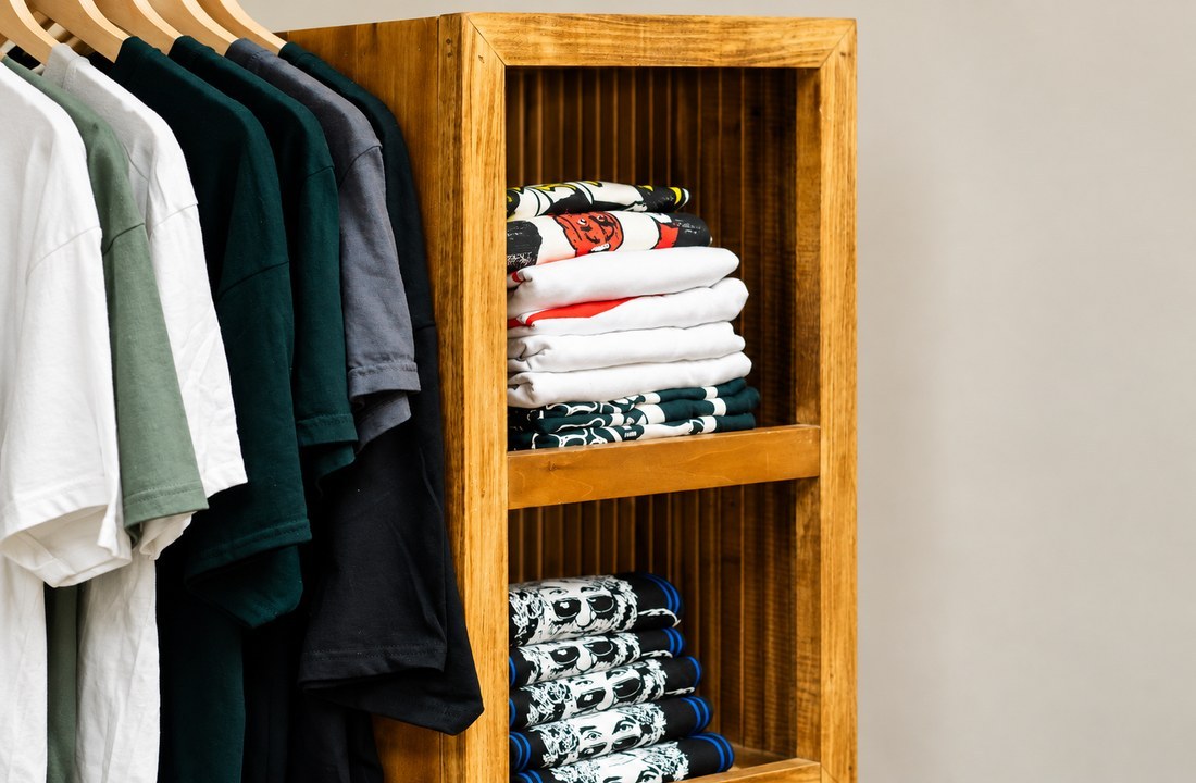 Folded graphic T-shirts on wooden shelves beside plain tees on a rail