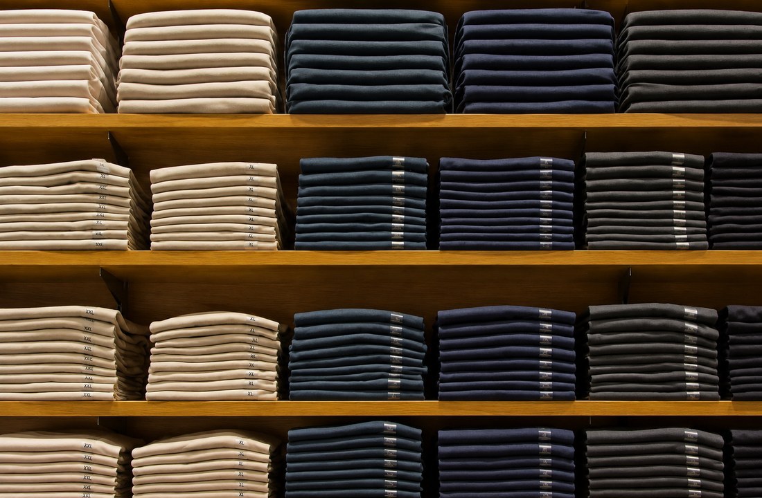 Folded beige and dark T-shirts separated into stacks on wooden shelves