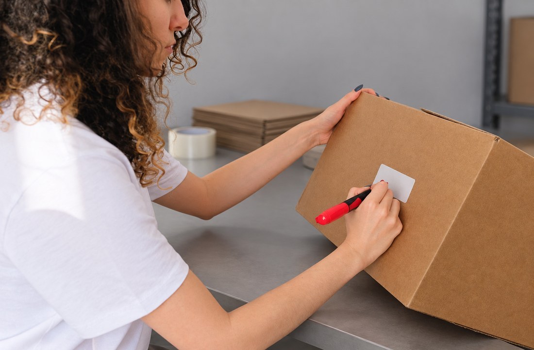 Woman in a white T-shirt marking a plain carton label with a red pen