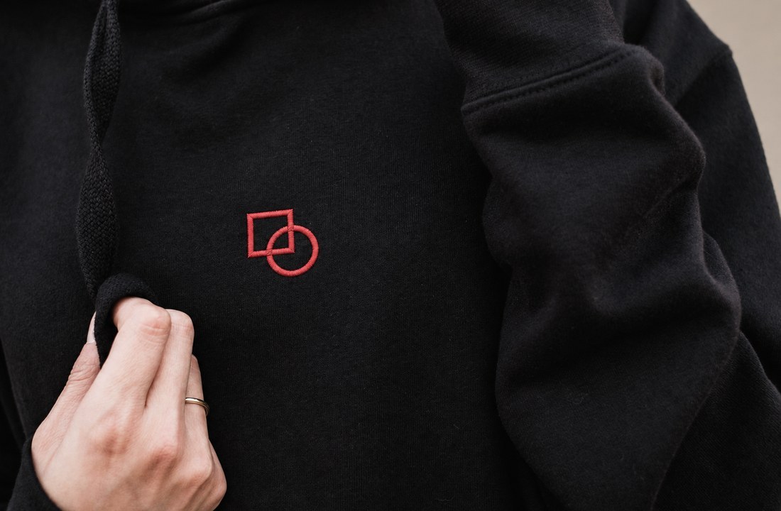 Small red geometric embroidery on a black sweatshirt held near the chest