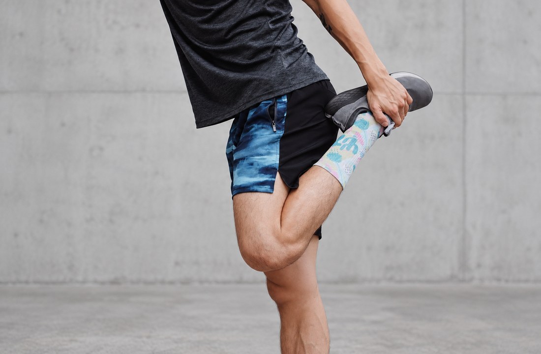Person stretching in black and blue shorts against a concrete wall