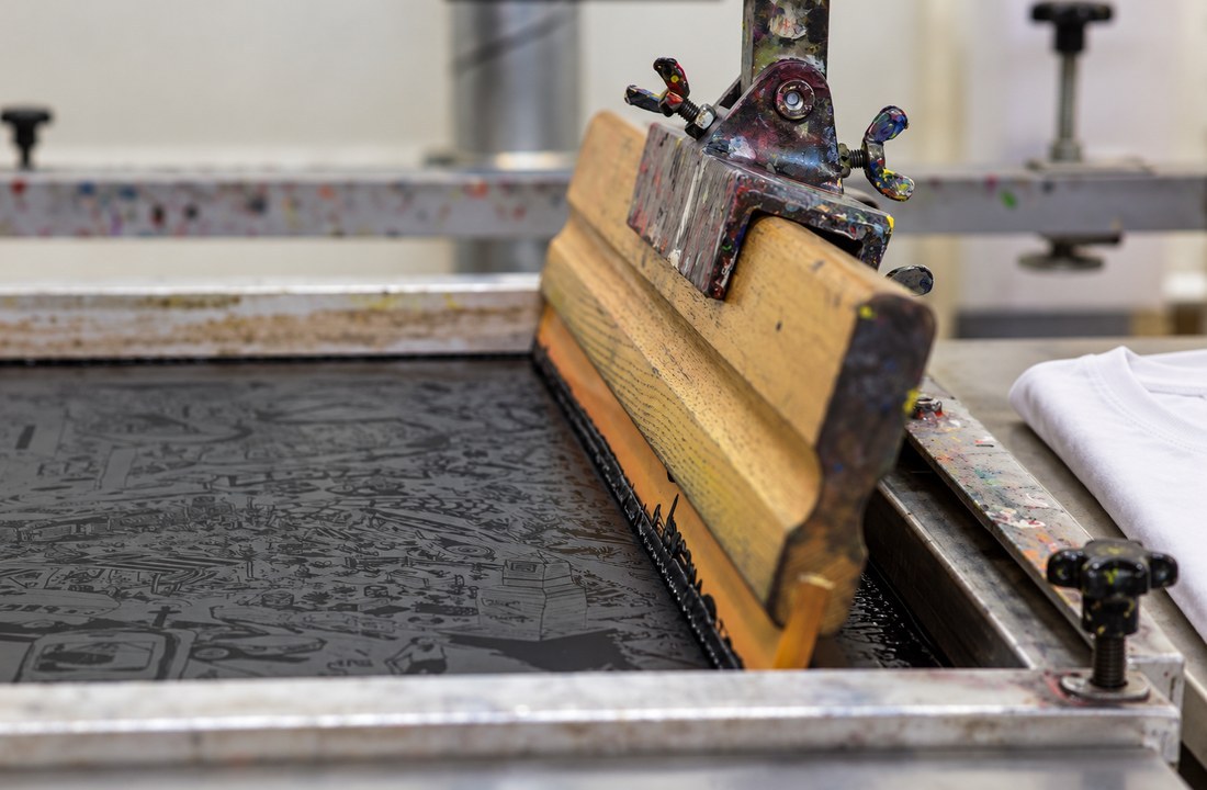 Close-up of a screen-printing squeegee beside a folded white T-shirt