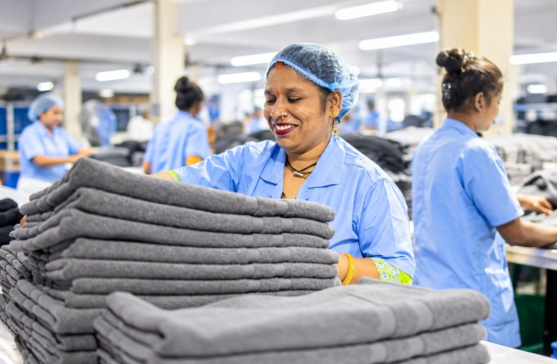 Worker organizing folded grey garments on an apparel worktable